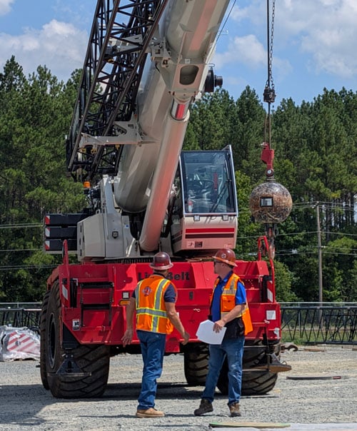 Two construction professions stand in front of a parked mobile crane.